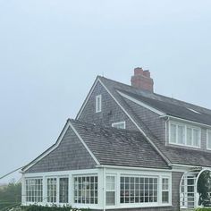 a white house with a gray shingled roof and large windows on the side of it