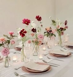 the table is set with pink and white flowers in vases, candles, and plates