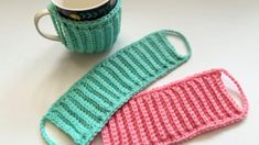 two crocheted mug cozys sitting next to each other on a white table