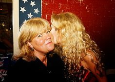 two women are kissing each other in front of an american flag and red white and blue background