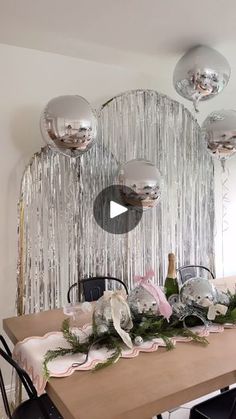 the table is set with silver balloons and greenery