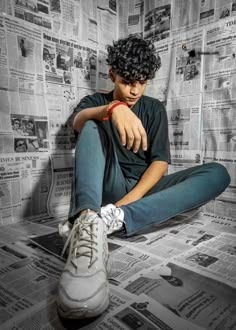 a young man sitting on the floor in front of newspaper wallpaper with his foot up