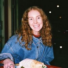 a woman sitting at a table with a sandwich in front of her and smiling for the camera