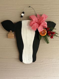 a black and white cow with a red bow on it's head hanging from a wall