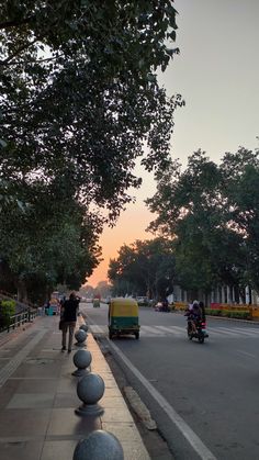 people are walking down the sidewalk in front of some parked cars and motorcycle riders at sunset