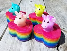 four small toy animals sitting on top of pink and blue heart shaped soaps with rainbow colors