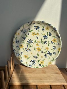 a white plate with blue and yellow flowers on it sitting on top of a wooden table