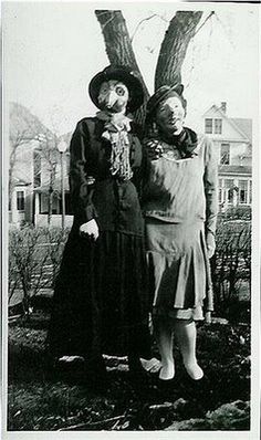 two women standing next to each other in front of a tree and houses on the other side