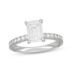 an emerald cut diamond engagement ring with diamonds on the band and side stones in white gold