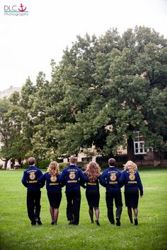 a group of people in blue jackets walking through the grass near a large green tree