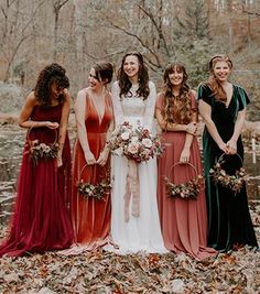 a group of women standing next to each other in front of a pond holding bouquets