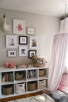 a white shelf with baskets and pictures on it next to a pink canopy over the bed