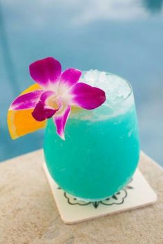 a blue drink with a flower on the rim next to a swimming pool and water