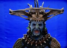 a man with blue face paint and antlers on his head is standing in front of a blue background