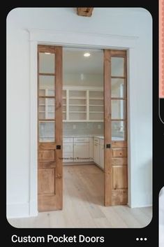 an open wooden door leading to a kitchen with white cabinets and wood floors in the background