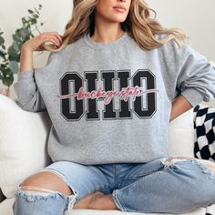 Show off you love for the state of Ohio with our trendy and classic varsity inspired design on the Gilden Unisex crewneck sweatshirt. With Ohio in a collegiate varsity font and buckeye state in all cursive through the center, Ohioans at heart will love this cozy sweatshirt. This makes the perfect gift for yourself or your family and friends. This sweatshirt will soon become your favorite thing to wear on those cold Ohio winter days.  Ideal for any situation, a unisex heavy blend crewneck sweatshirt is pure comfort. These garments are made from polyester and cotton. This combination helps designs come out looking fresh and beautiful. The collar is ribbed knit, so it retains its shape even after washing. There are no itchy side seams on these sweaters.  .: Made with a medium-heavy fabric ble College Crew Sweatshirt With Slogan, School Spirit Tops With Letter Print For Campus, School Spirit Letter Print Tops For Campus, Campus Letter Print Tops With School Spirit, Campus Letter Print Tops For School Spirit, Varsity Lettering Sweatshirt For Campus, Varsity Sweatshirt With Lettering For Campus, College Crew Neck Sweatshirt With Slogan, College School Spirit Sweatshirt With Text Print