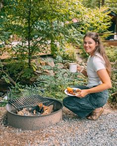 a woman sitting on the ground next to an open fire pit holding a plate of food