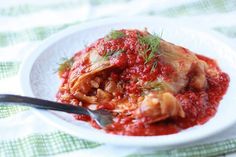 a white plate topped with meat covered in sauce and garnished with fresh herbs