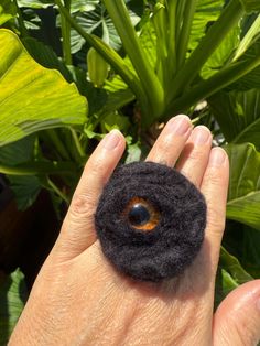 a woman's hand holding a black felt ring with an orange center surrounded by green leaves