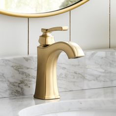 a gold faucet sink in front of a white marble counter top with a round mirror above it