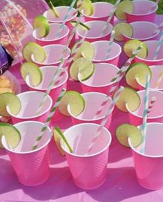 pink cups with limes, strawberries and lemon slices on them sitting on a table