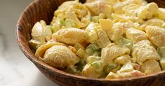 a wooden bowl filled with macaroni salad on top of a white countertop