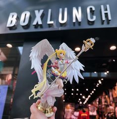 a person holding up a toy in front of a box lunch sign with an angel figurine on it