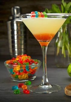 a martini with gummy bears in the glass next to it and a bowl full of candy