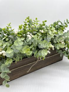 a wooden planter filled with green and white flowers on top of a white table