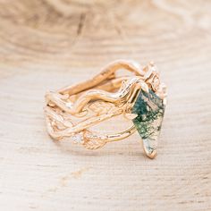 three gold rings with green and white stones on them sitting on a piece of wood