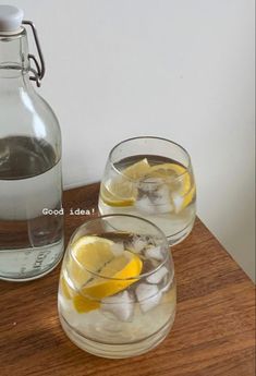 two glasses filled with ice and lemons next to a pitcher of water on a table