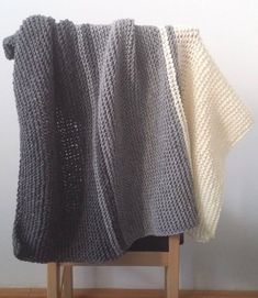 a gray and white knitted blanket sitting on top of a wooden chair next to a wall