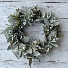 a wreath with white flowers and green leaves hanging on a wooden wall, ready to be used as an ornament