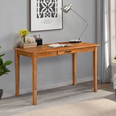 a wooden desk with a lamp on it in front of a gray wall and potted plant