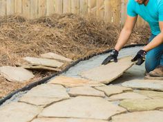 a man in blue shirt and black gloves working on stone walkway