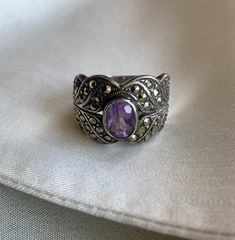 Stunning art deco style silver ring with encrusted in marcasite with an oval amethyst coloured glass stone. This one is hard to date - it looks to possible have a hallmark/stamp but it is hard to make out. It has a beautiful deco style and could be from the 20s-40s.  This would be a lovely engagement ring or celebratory gift...to yourself or someone else! Condition: Great condition with some scratching as to be expected from wear  Label: 925 Content: silver, marcasite, amethyst coloured stone Size on Label: n/a Measurements: Size 6 *IMPORTANT NOTE: All measurements are taken with the garment lying flat and then doubled. Please leave some wiggle room for comfort. *SALES ARE FINAL: Please make any inquiries prior to purchase. All clothing is pre-owned unless specified and comes with a certai Vintage Oval Marcasite Rings, Vintage Marcasite Oval Rings, Vintage Oval Marcasite Jewelry, Art Deco Silver Oval Rings, Silver Oval Art Deco Rings, Silver Victorian Amethyst Oval Ring, Art Deco Silver Amethyst Jewelry, Art Deco Amethyst Silver Jewelry, Silver Victorian Oval Amethyst Ring