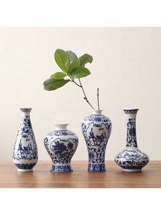 three blue and white vases sitting on top of a table next to a plant