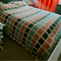 a crocheted blanket on top of a bed in a room with red curtains