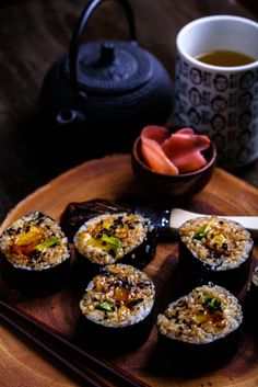 some sushi is sitting on a wooden plate next to a teapot and cup