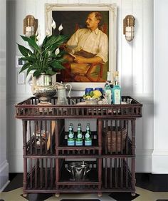 a painting hangs on the wall next to a table with bottles and glasses in front of it