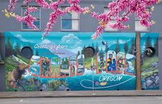 a mural on the side of a building with trees and flowers in front of it