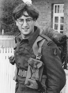 black and white photo of young man in uniform with back pack on shoulder, smiling at camera