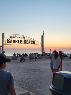 people standing on the beach at sunset with a welcome to sauble beach sign in the background