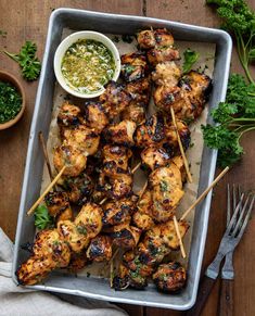 grilled chicken skewers on a tray with dipping sauce and parsley greens