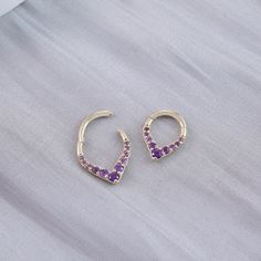 two pairs of earrings with purple stones in the shape of an open heart on a white background