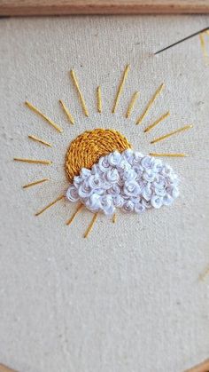 an embroidered sun and cloud on a piece of fabric in a wooden frame with thread spools