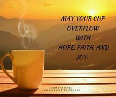 a coffee cup sitting on top of a wooden table next to a mountain range with the words, may your cup overflow with hope, faith, and joy