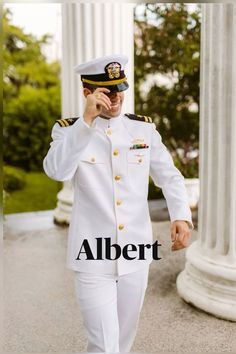 a man in uniform is talking on his cell phone while walking down the street with columns behind him