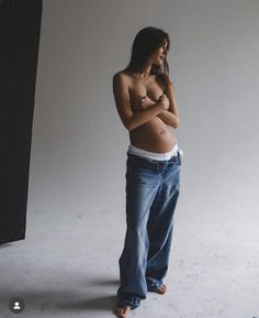 a pregnant woman standing in front of a white wall with her arms crossed and looking at the camera