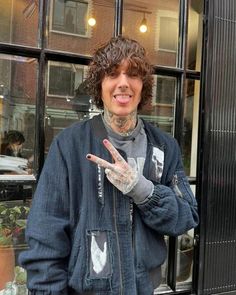 a man with tattoos standing in front of a window making the peace sign and holding his hand up